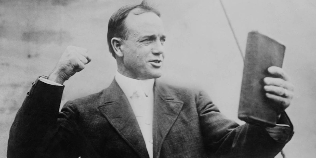 Man in suit holding a book and making a fist.