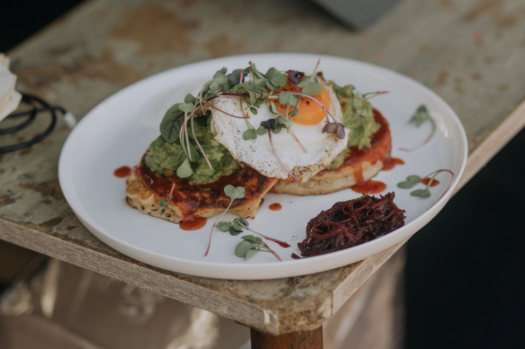 Savory breakfast with fried egg, avocado, microgreens, and sauce on toast.