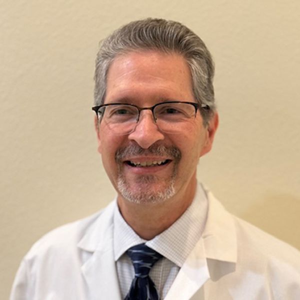 Smiling male doctor wearing glasses and white coat.
