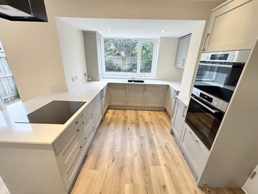 Modern kitchen with gray cabinets, white countertops, and wooden flooring.