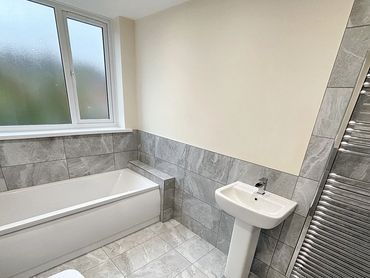 Modern bathroom with gray tiled walls and floor, white fixtures, and a chrome towel radiator.