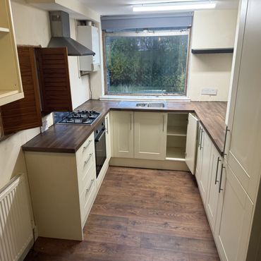 Modern U-shaped kitchen with wooden countertops and cream cabinets under large window.