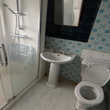 A small bathroom with white sink, toilet, and shower area.