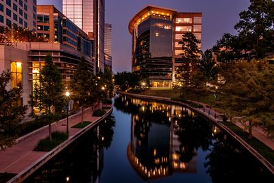 Evening cityscape with illuminated buildings reflecting on a calm canal.