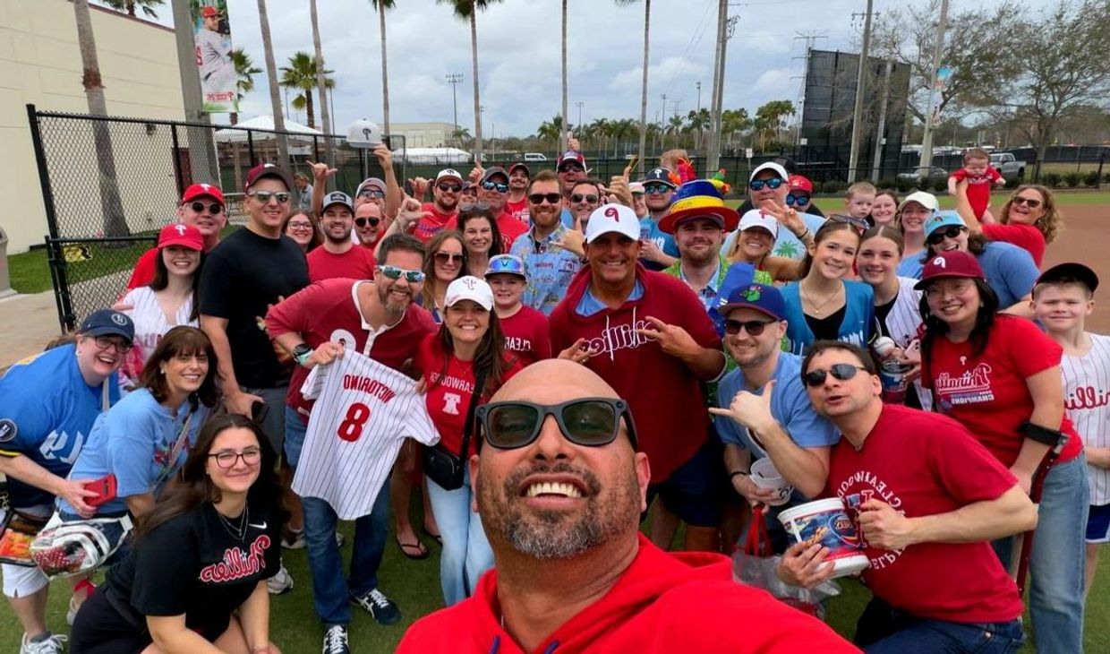 Large group of baseball fans smiling and posing for a selfie at a sports field.