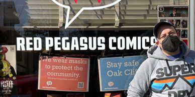 A photo of Comic Book Shop owner Gabriel Mendez in front of his store wearing a mask.