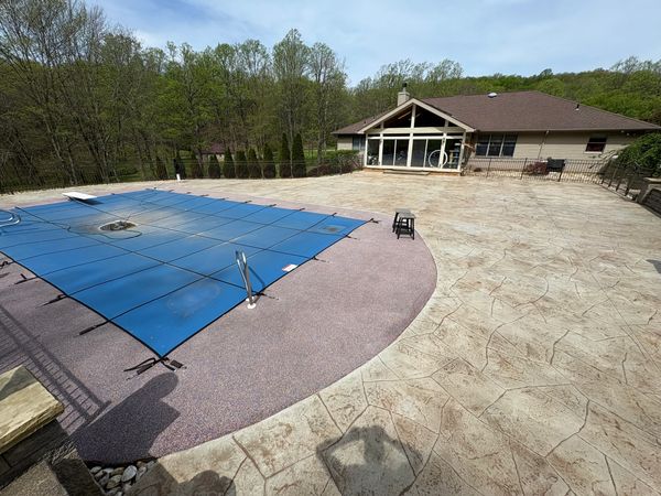 Covered pool in a spacious backyard with a large patio and a house in the background.