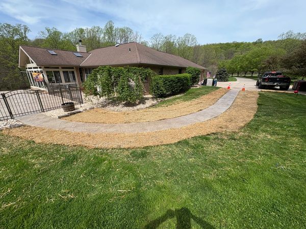 Newly laid concrete pathway curves around a house with fresh straw covering the adjacent soil.
