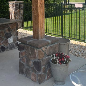 Stone pillar with wooden post next to a flower pot on a patio.