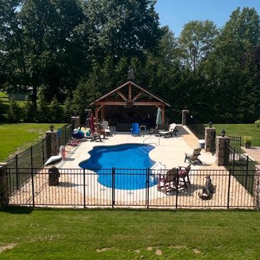 Backyard with a fenced-in pool and a covered patio area surrounded by greenery.