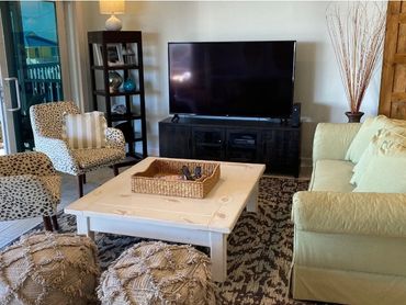 Cozy living room with patterned chairs, a green sofa, and a large TV on a black stand.