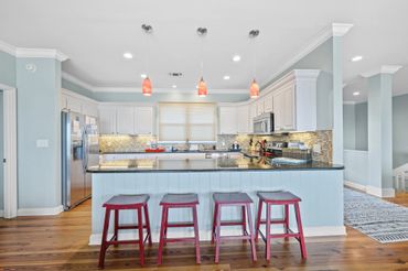 Modern kitchen with four red stools and pendant lights over a granite island.