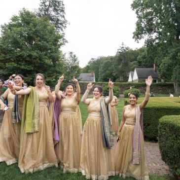 Group of women in matching gold dresses raising their hands outdoors.