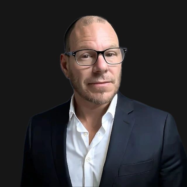 Dr. Joey Pagano wearing glasses, a navy suit jacket, and a white shirt.