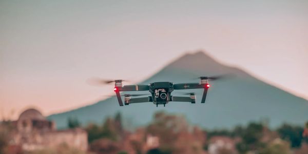 A drone flying with a mountain backdrop during sunset.