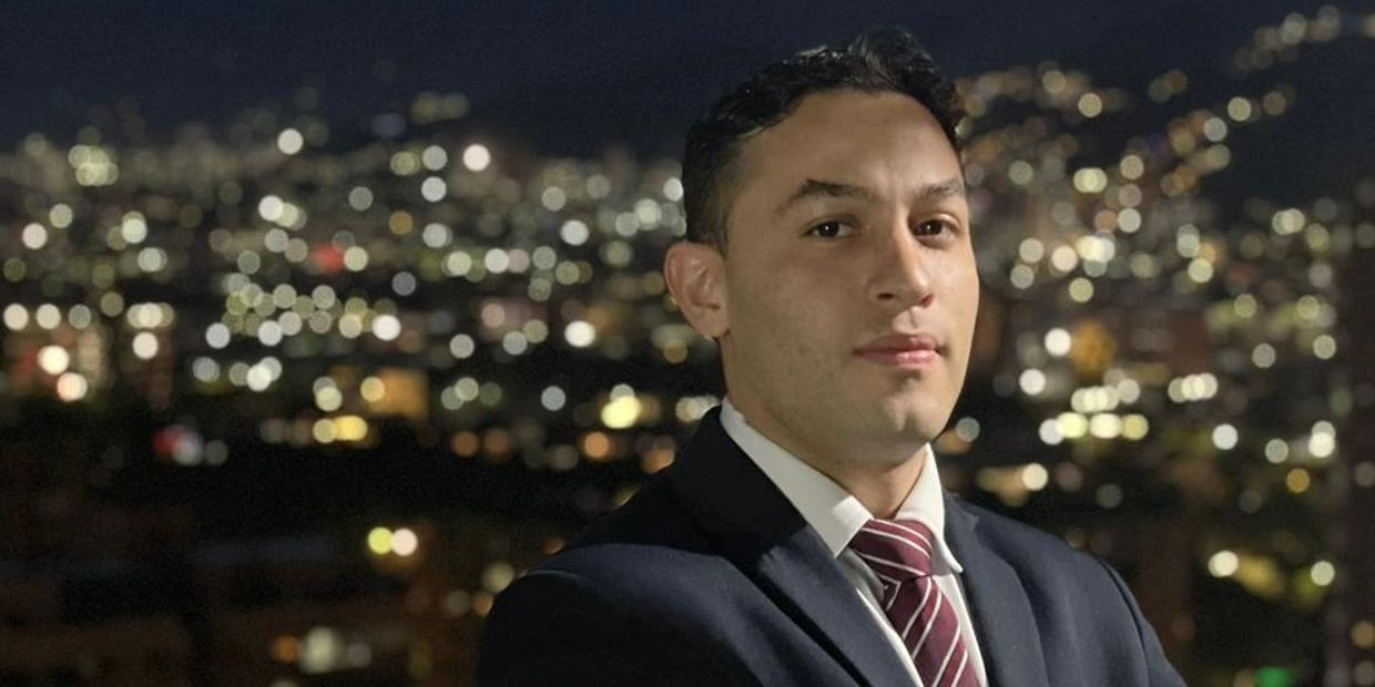 Man in suit at night with city lights background.