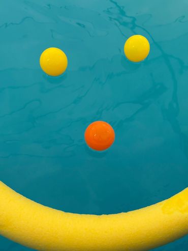 Smiley face made with balls and a pool noodle floating on water.