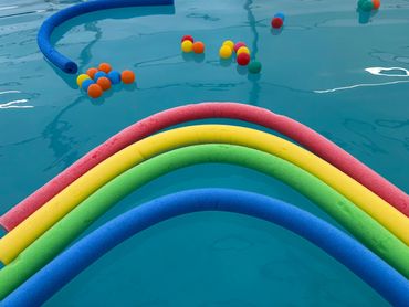 Colorful pool noodles and floating balls in a swimming pool.