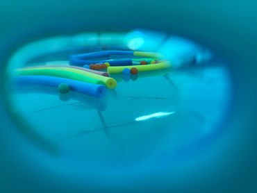 Colorful pool noodles and balls floating in a pool, viewed through an underwater lens.