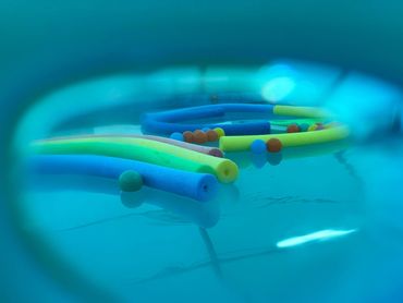 Colorful pool noodles and balls floating in a pool, viewed through an underwater lens.