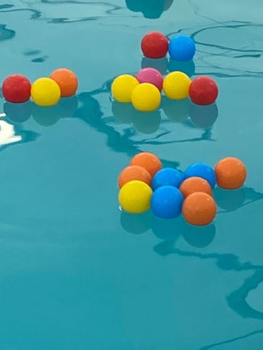 Colorful pool toys and balls floating on clear blue water in a pool.