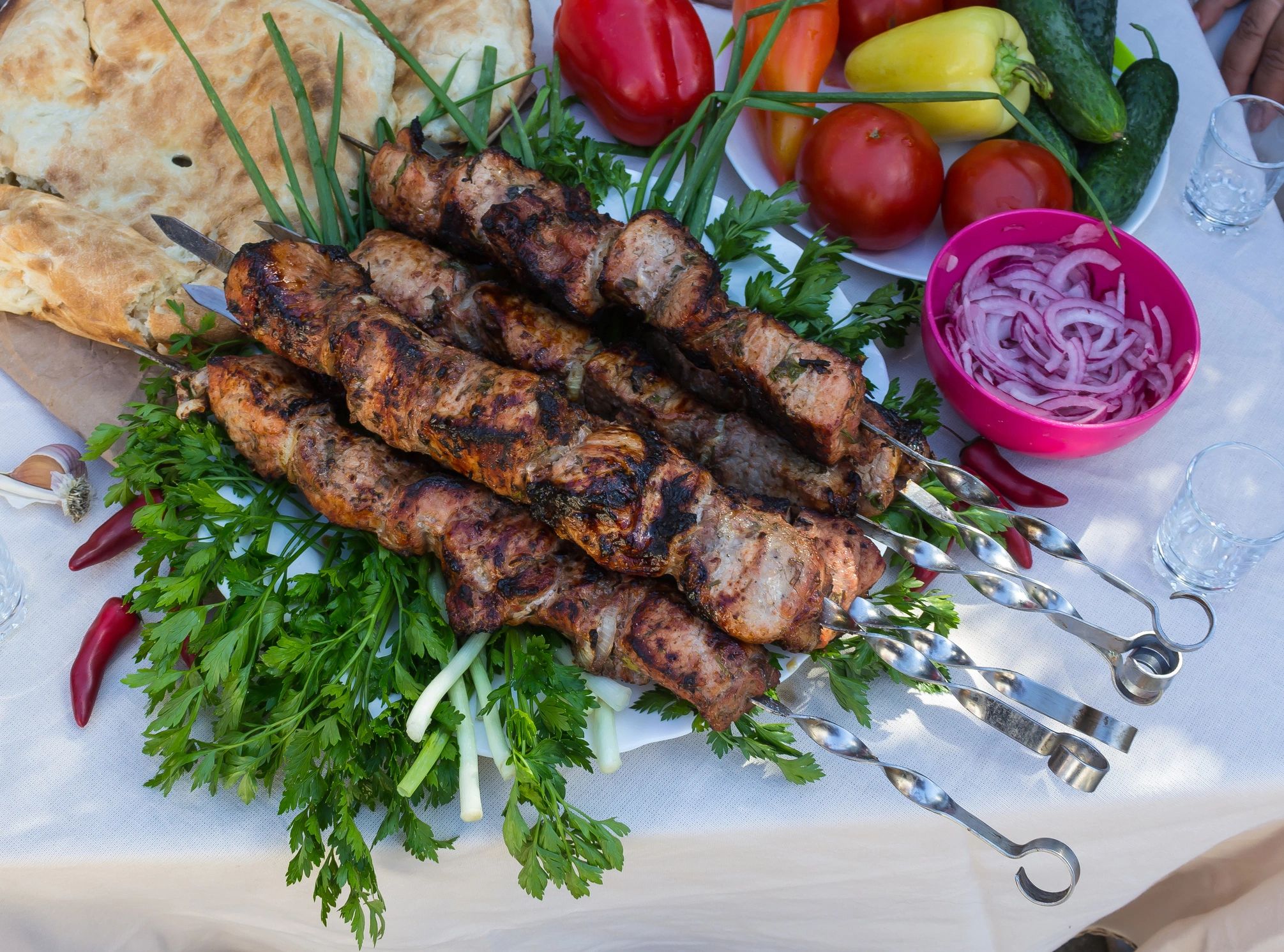 skewers of meat on a table in a garden with tomatoes, tortillas and vegetables