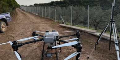 A large drone with six propellers on a dirt path near a fence and tripod.
