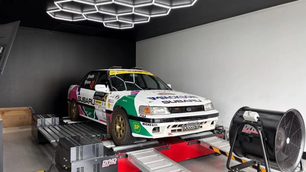 Subaru rally car on a dynamometer in a garage.