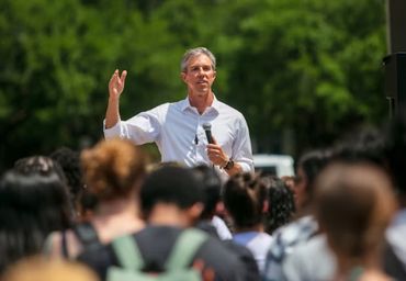 Man speaking to a crowd outdoors with a microphone.