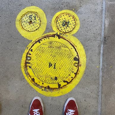 3 yellow circles painted on metal hole-covers on the sidewalk that looks like micky mouse.