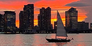 Sunset skyline of Jersey City viewed from NY. Sailboat on the Hudson River.