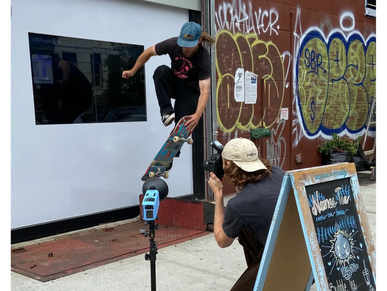 A photographer capturing a performance of a skateboarder doing a trick in front of a pharmacy.