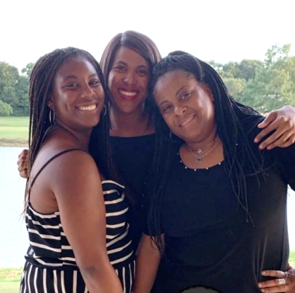 Three women smiling outdoors near water.