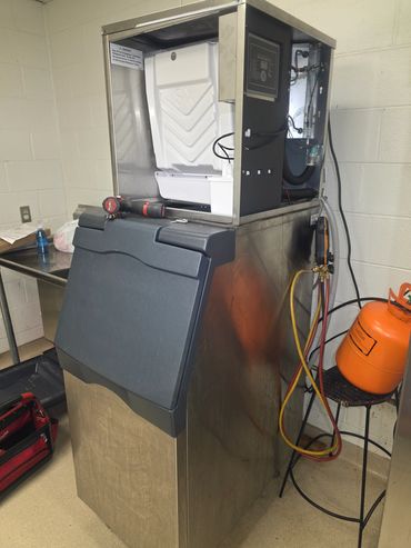 A commercial ice machine undergoing maintenance with tools and refrigerant tank nearby.