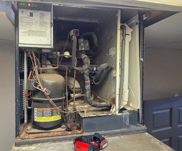 Old and dusty ice machine with exposed components and a worker's tool on the counter.
