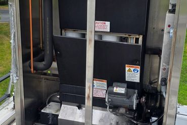 An open HVAC unit with visible copper pipes and a red tool bag nearby.