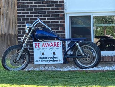 Motorcycle with a safety sign encouraging awareness of motorcycles on the road.