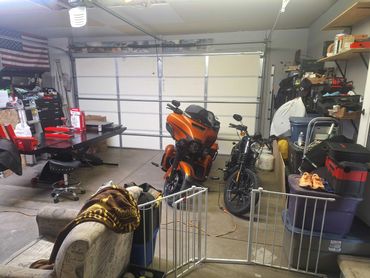 Two motorcycles parked inside a cluttered garage with various tools and storage items.