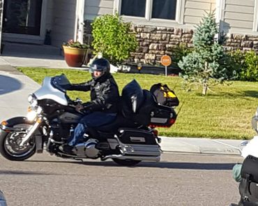 A motorcyclist rides a fully loaded touring bike in a suburban neighborhood.