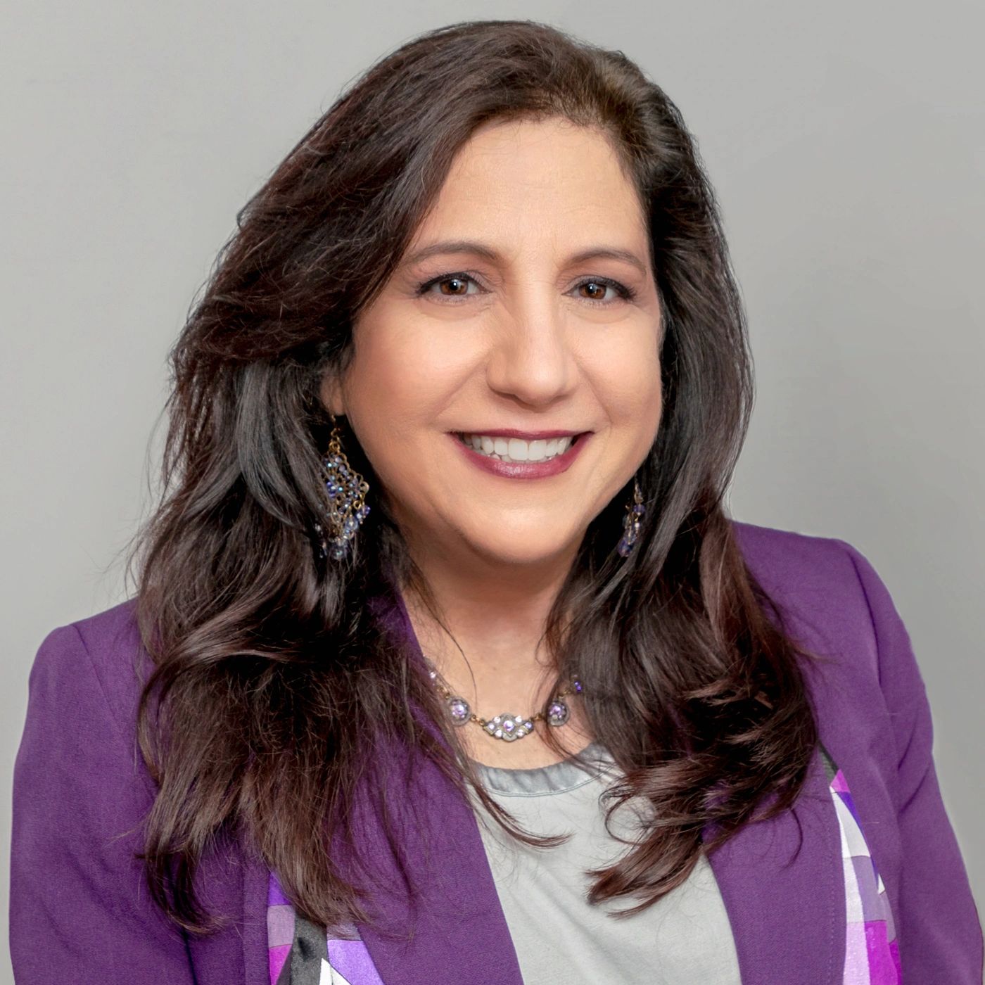Smiling woman with long dark hair wearing a purple blazer and jewelry.