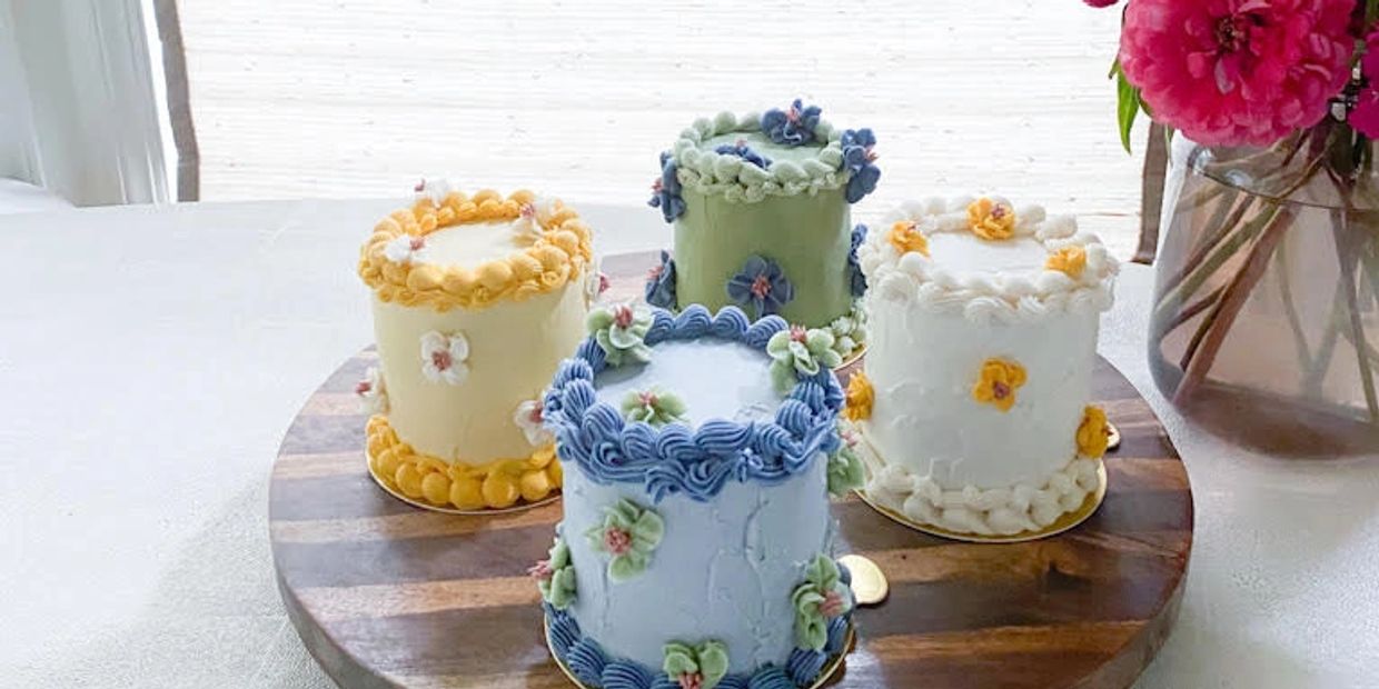 Four small floral decorated cakes on wooden board.