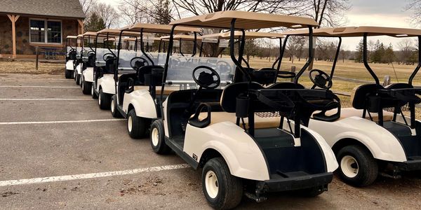 A line of white golf carts parked in a row on a paved lot.