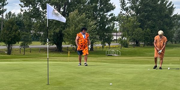 Two men in Flintstones costumes play golf on a sunny day.