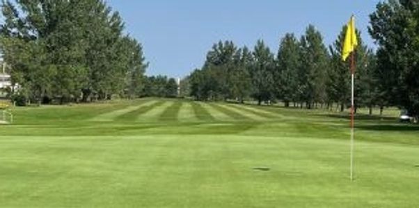 Golf course green with a yellow flag and striped fairway under a clear blue sky.