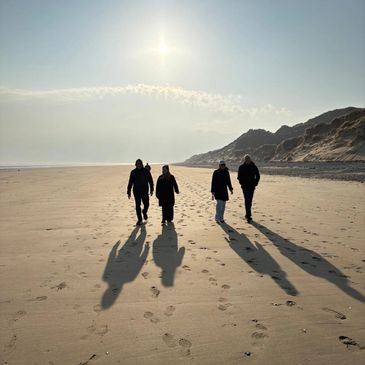 Four people walking on a sunny beach casting long shadows.