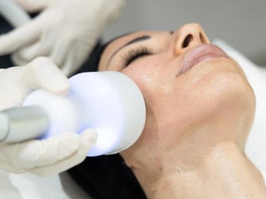 Woman receiving facial treatment with a handheld device.