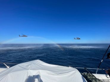 two miltary helicopters flying close to the ocean surface