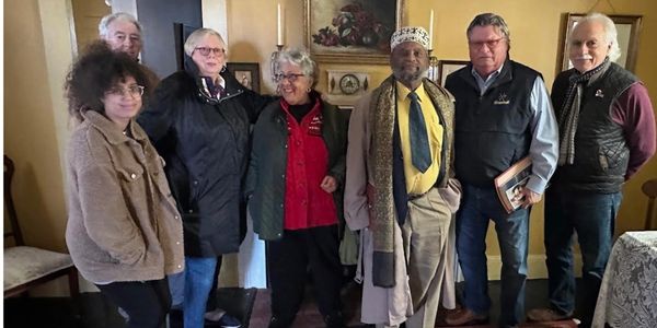 Group of seven people posing indoors, dressed warmly.