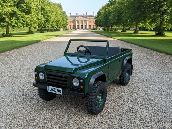 Small green off-road vehicle on gravel path with mansion in background.