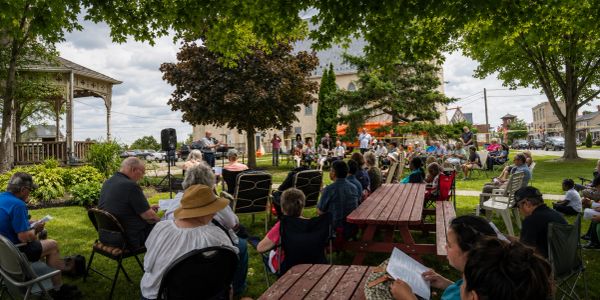 Community event with people seated outdoors under trees.